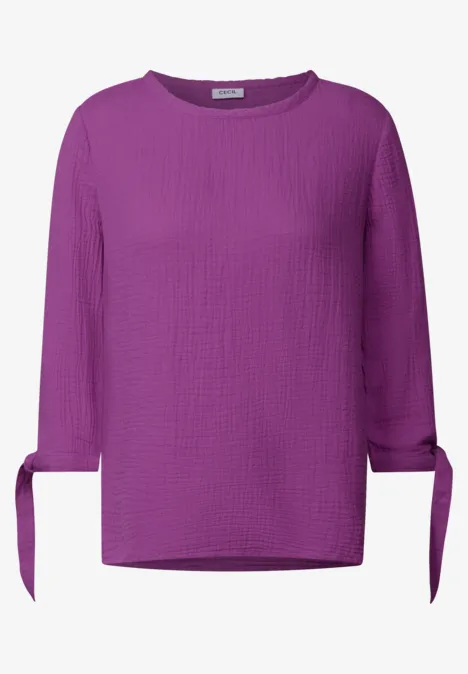 Lila Bluse mit 3/4-Ärmeln und Knoten an den Ärmelenden.